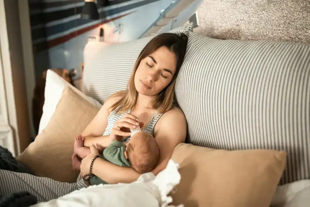 Young mom resting on a couch feeding her newborn baby